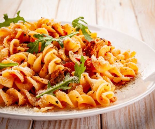 Fusilli with pork, sauce and vegetables on color gradient background